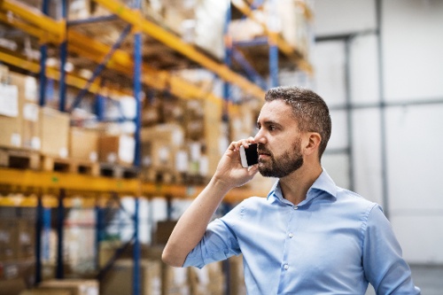 Deskless worker in a warehouse talking to coworkers on his mobile phone