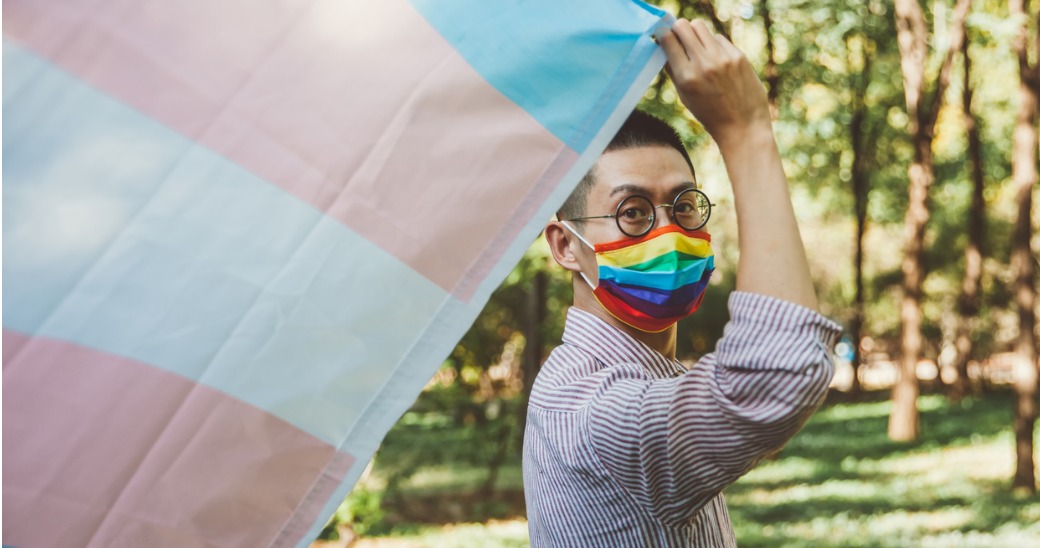 Person with rainbow mask and Transgender Pride flag